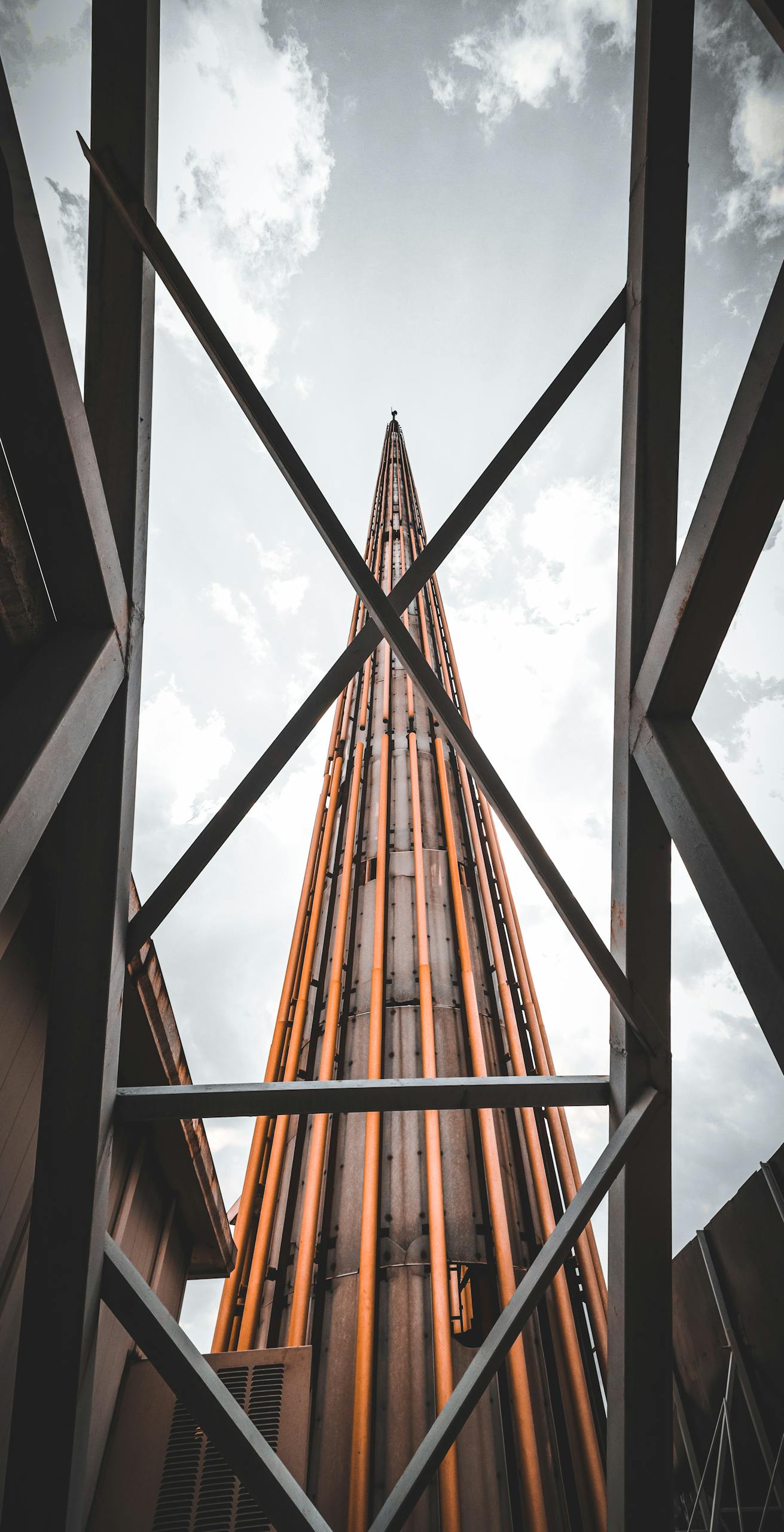 Dramatic view of a tall modern structure framed by steel beams against a cloudy sky.